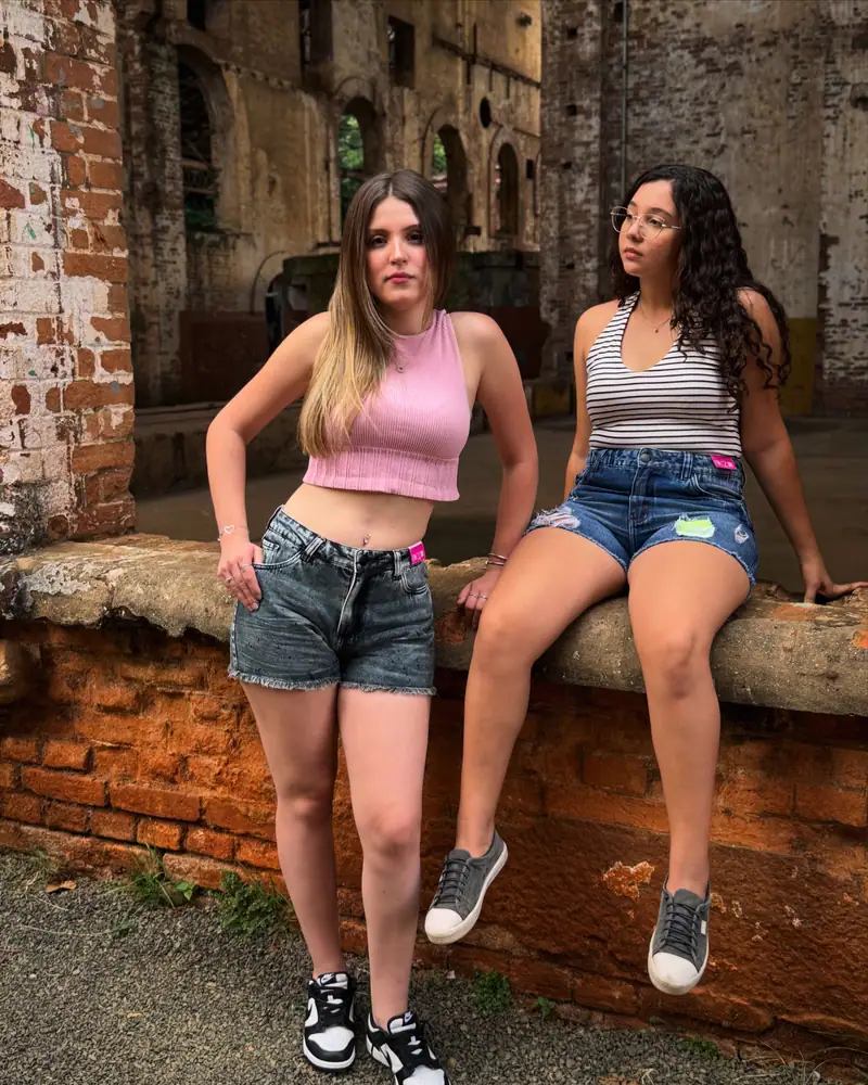 Duas amigas com shorts jeans CVHM sentadas em um muro de tijolos