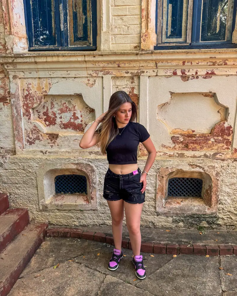 Mulher com short jeans escuro CVHM em frente a uma parede antiga
