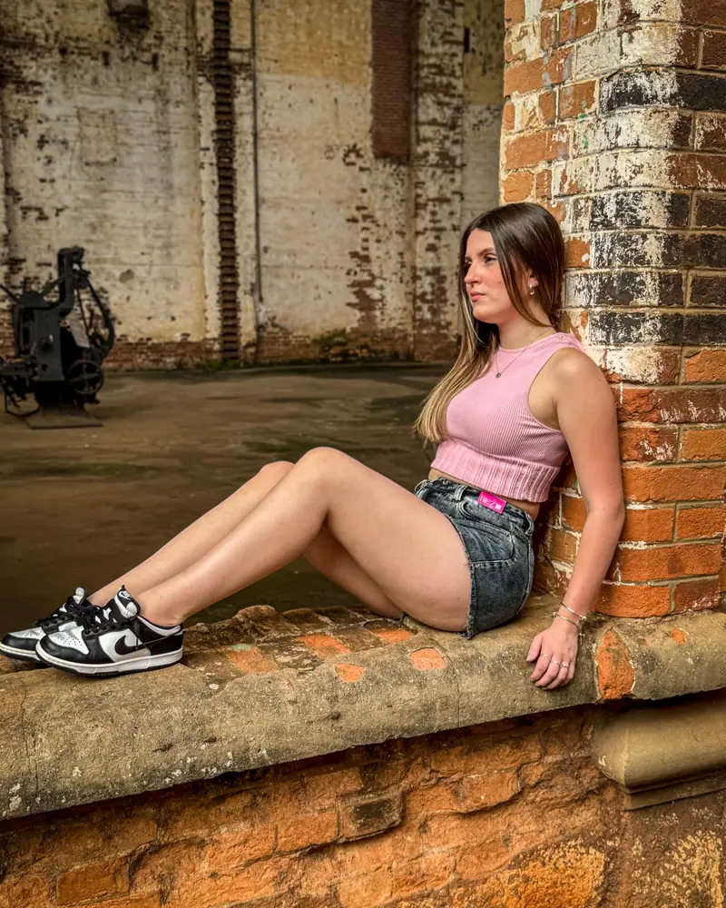 Mulher de short jeans CVHM e tênis sentada em um muro de tijolos