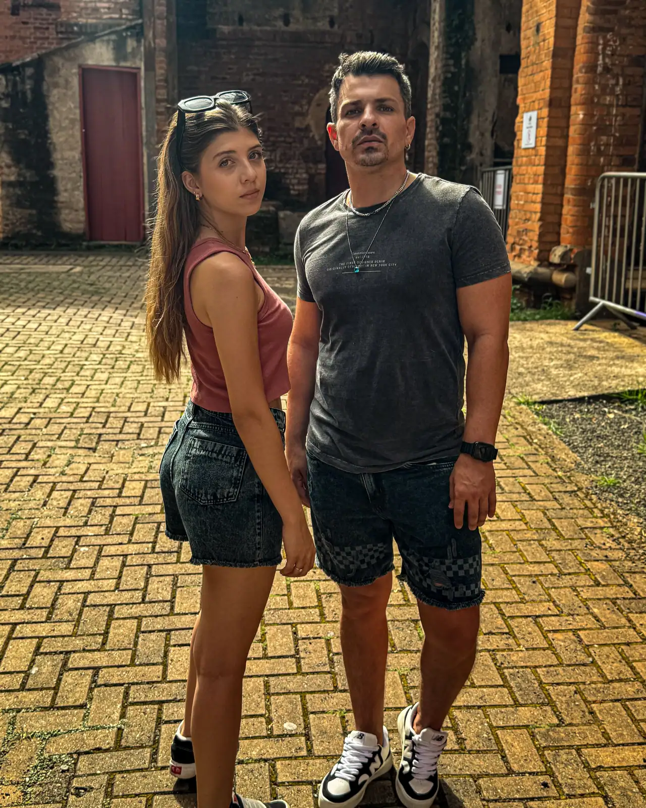 Casal com shorts jeans CVHM sorrindo em um pátio de tijolos