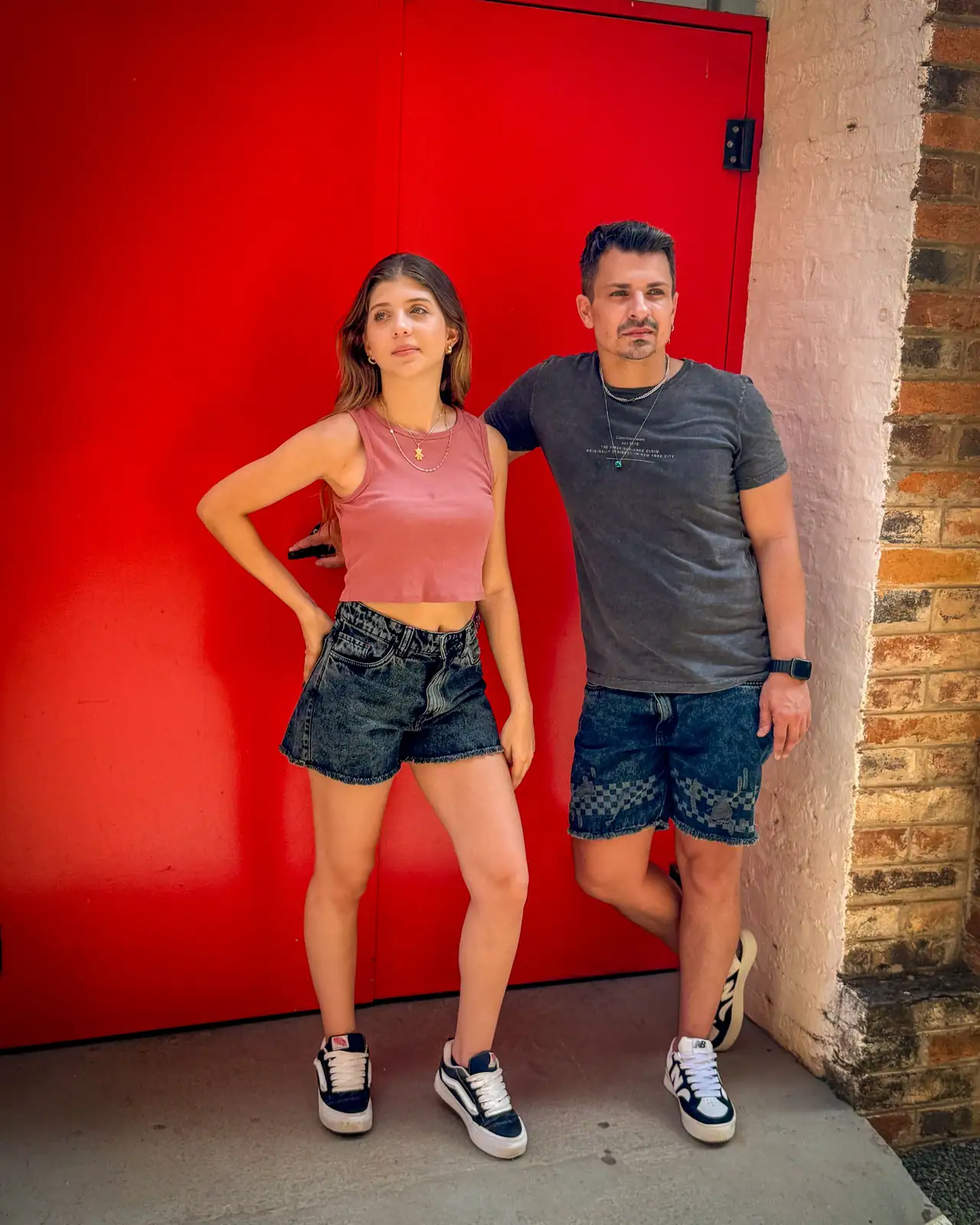 Casal com shorts e bermuda jeans CVHM em frente a uma porta vermelha