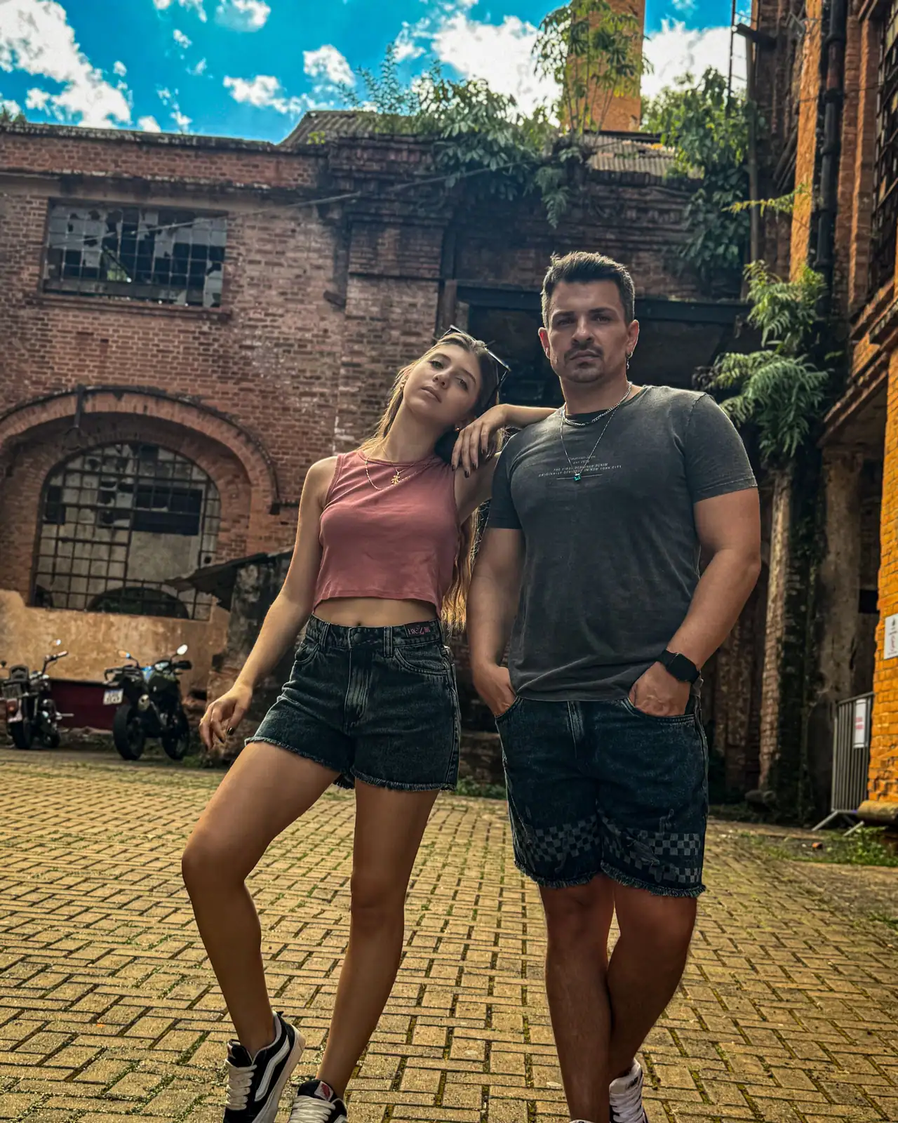 Casal vestindo shorts e bermuda jeans CVHM em uma fábrica antiga de tijolos